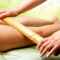 Close up of therapist hands massaging female legs with bamboo stick.